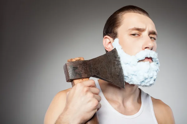 Attractive young bearded guy shaves with hatchet — Stock Photo, Image