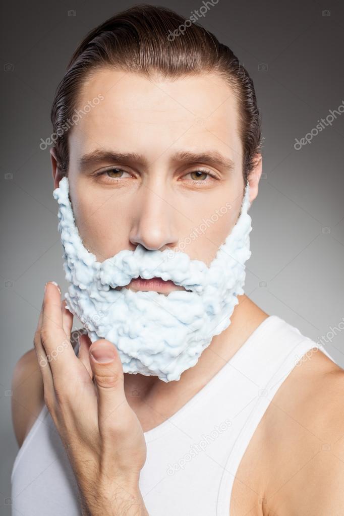 Attractive young bearded man shaves with joy