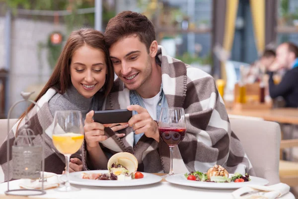 Hermosa joven pareja amorosa está utilizando el teléfono en la cafetería — Foto de Stock