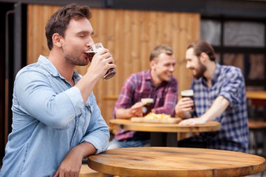 Cheerful young guy is swigging lager in bar clipart