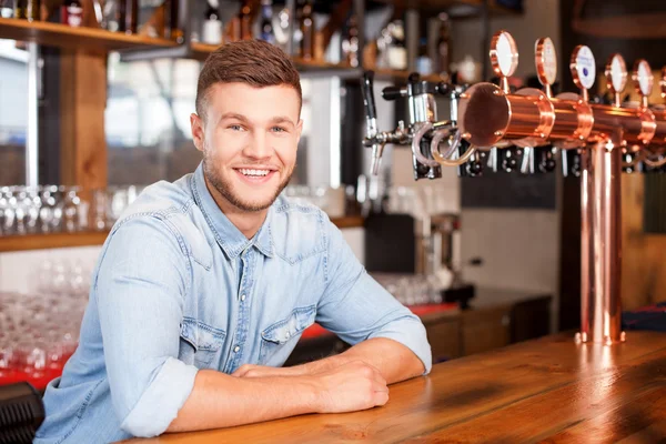 Jovem barman alegre está esperando pelo cliente no pub — Fotografia de Stock