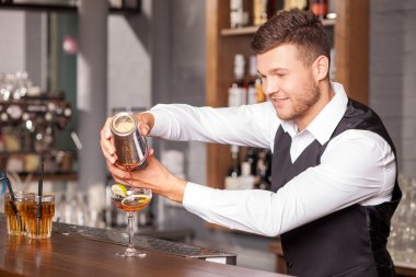 Cheerful young barman is making cocktail in bar