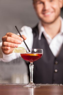 Cheerful young barman is making beverage in bar