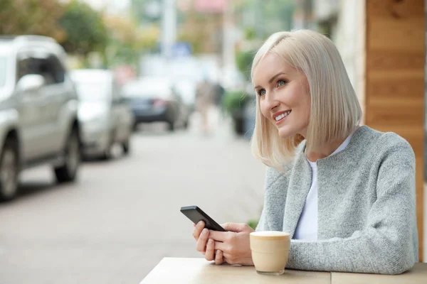 Mujer rubia alegre con teléfono en la cafetería — Foto de Stock