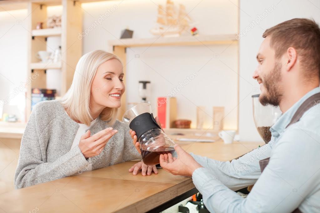 Cheerful young cafe owner in serving female customer