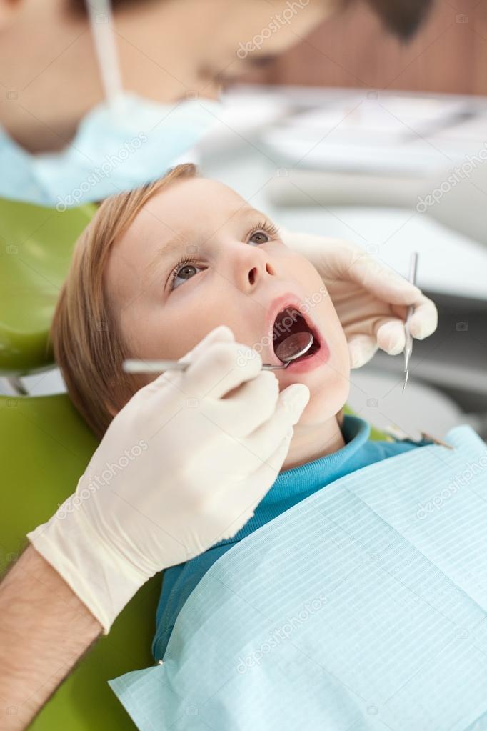Cheerful young dentist is checking tooth of child