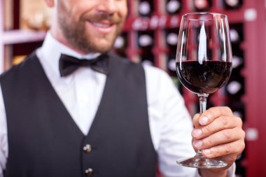Cheerful young male waiter is carrying wineglass