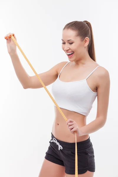 Jovem menina magra alegre está tomando medidas de seu corpo — Fotografia de Stock