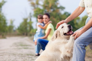 Cheerful friendly family and puppy are resting in park