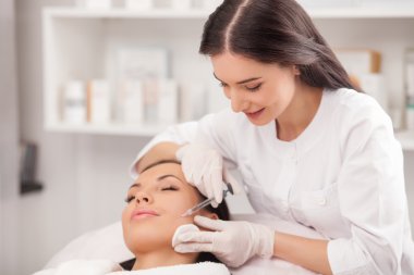 Attractive expert beautician is injecting female face