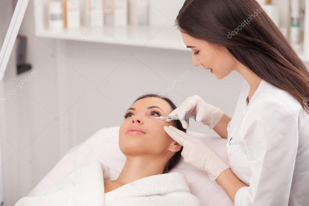 Cheerful young cosmetologist is making botox procedure