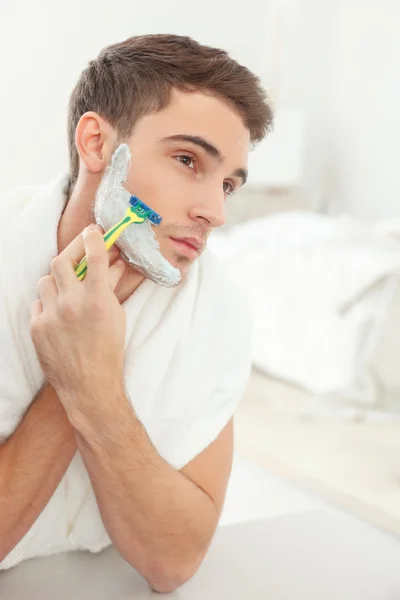 Attractive guy shaves with joy in bathroom