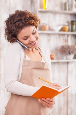 Cheerful female cafe worker is making notes