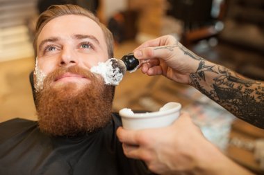 Cheerful bearded hipster is visiting his hairdresser