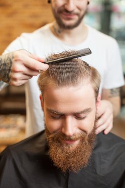 Cheerful bearded hipster is getting a cool hairstyle