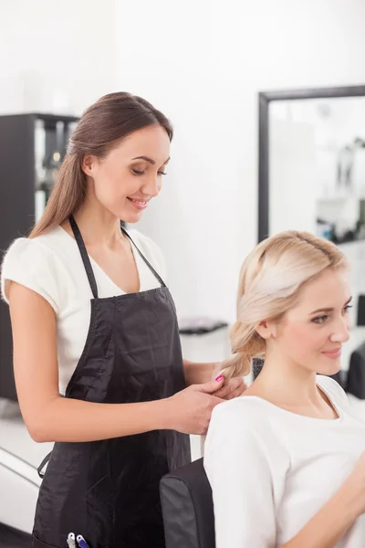 Skillful young hairstylist is making braid for customer — Stok fotoğraf