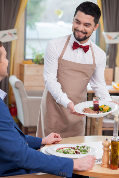 Веселый работник кафе обслуживает клиента
