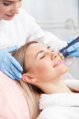 Cheerful young therapist is doing photorejuvenation of skin