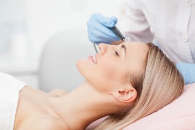 Skillful young cosmetologist is treating her patient