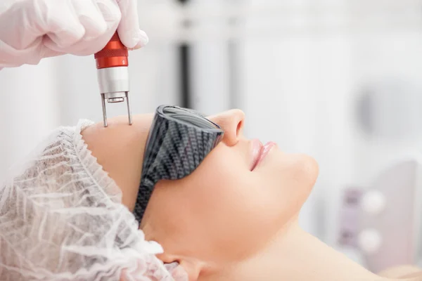 Cosmetologista hábil alegre está tratando o rosto feminino — Fotografia de Stock