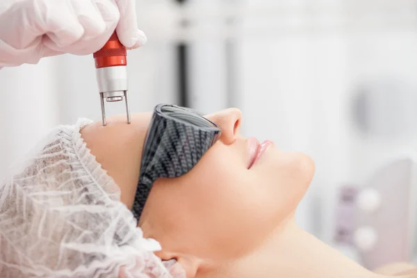 Cheerful skillful cosmetologist is treating female face — 스톡 사진