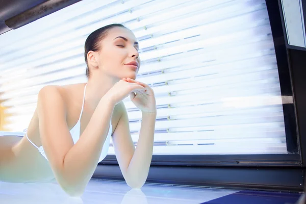 Cheerful young woman is getting treatment in solarium — Stockfoto