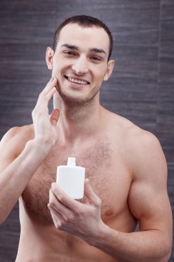 Attractive young man is using moisturizer after shaving