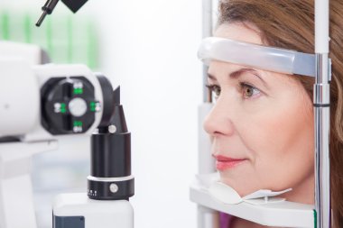 Mature lady is looking into eye test machine