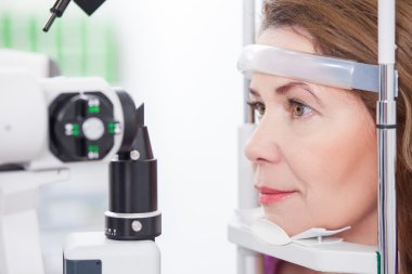 Mature lady is looking into eye test machine clipart
