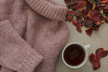 Sıcak pembe kazak, bir fincan mis kokulu çay ve gri arka planda renkli sonbahar yaprakları.