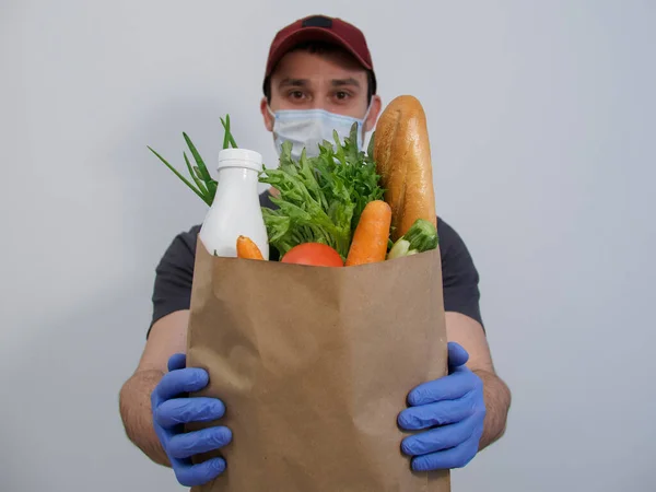 Safe delivery of food to your home in a pandemic, quarantine, self-isolation. Courier holds a package of groceries in blue gloves