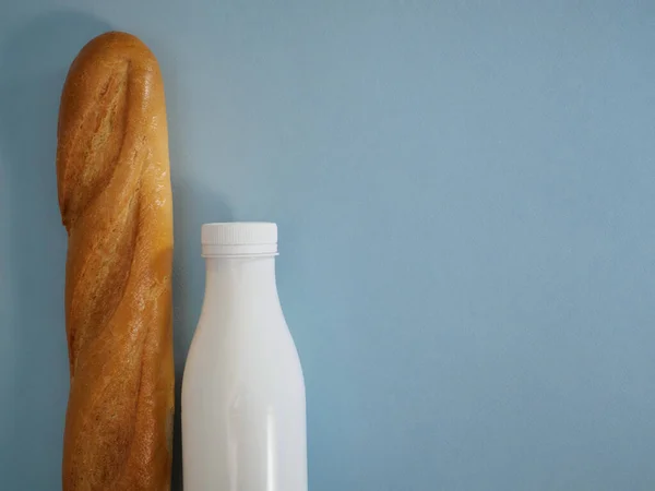 Φρέσκια γαλλική μπαγκέτα και ένα μπουκάλι γάλα φάρμας ή κεφίρ σε γαλάζιο φόντο με χώρο για κείμενο στα δεξιά. Επίπεδη lay τροφίμων, κορυφαία άποψη, βασικά τρόφιμα — Φωτογραφία Αρχείου