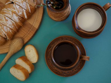 Yeşil arka planda el yapımı antika el yapımı toprak parçaları. Sade kahve, süt, taze hamur işleri, bir sürahi ekmek ve süt. Tablo ayarı üst görünüm, düz yatış