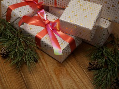 Tahta bir masada kırmızı kurdeleli Noel hediyeleri. Köknar kozalakları ve köknar dallarıyla Noel arkaplanı