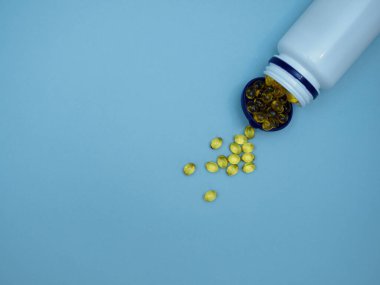 Sarı yumuşak kapsüller D vitamini, omega 3, 6, 9 plastik bir kavanozda ve mavi arkaplan üzerine yayılmış metin, üst görüş, düz yatış