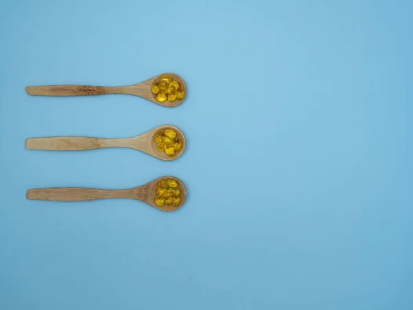 Vitamina D, E o cápsulas de aceite de pescado en cucharas de madera sobre fondo azul con espacio para copiar, vista superior, puesta plana — Foto de Stock