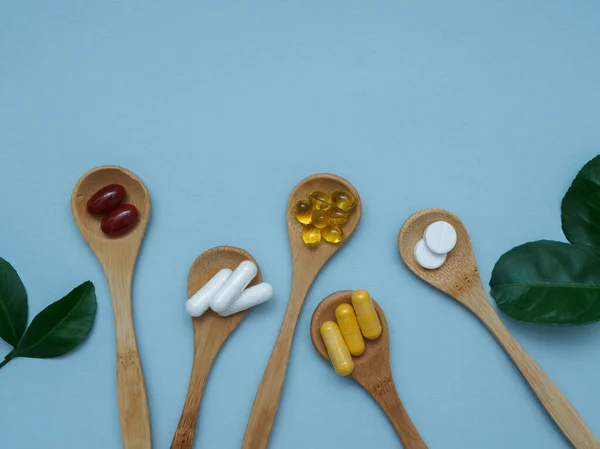 Mavi arka planda D, E, Omega 3 vitamini, kalsiyum, B vitamini tahta kaşıklarda fotokopi alanı ile yatıyordu.