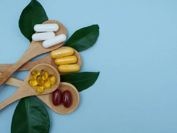 Vitaminer i kapslar i träskedar läggs ut på en blå bakgrund i form av en bukett med gröna blad. Omega 3, vitamin D, E, B, zink, kalcium i träskedar på en blå bakgrund med — Stockfoto