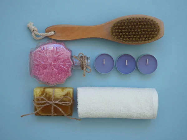 Sel de bain de mer, brosse de massage en cellulite, bougies de thé lilas, serviette blanche, savon fait à la main sur fond bleu, plat, vue sur le dessus. Accueil spa concept de traitement — Photo