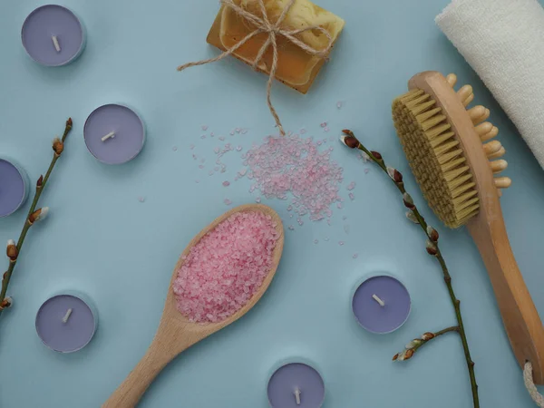 Evde spa tedavisi için bir takım eşyalar. Tahta kaşıkta deniz tuzu, kuru vücut masajı için fırça mavi arka planda çay yuvarlak mumlar. Düz yatıyordu