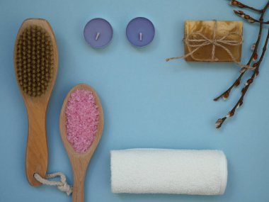 Kuru masaj fırçası, deniz tuzu banyosu, beyaz havlu, sabun, mavi arkaplanda kokulu mumlar fotokopi alanı, düz yatak, üst manzara