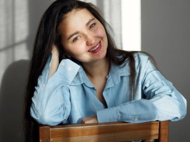 Mutlu gülümseyen Asyalı genç kadın portresi. Pencere kenarında oturan.