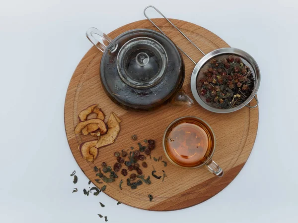 Gyógynövény tea szárított bogyókkal és almával, gyógynövények átlátszó teáskanna egy fa táblán fehér alapon, felülnézet — Stock Fotó