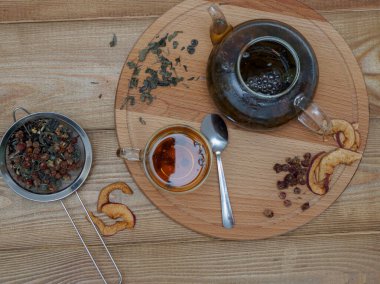 Sağlıklı siyah çay, otlar ve şeffaf bir çaydanlıkta kurumuş böğürtlen ve ahşap arka planda bir fincan, üst manzara. Sabah çayı, rahatlama.