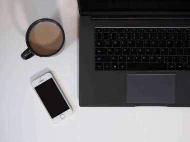 Bilgisayarlı beyaz ofis masası, mesaj için siyah ekranlı akıllı telefon, bir fincan kahve. Üst manzara, düz uzanma