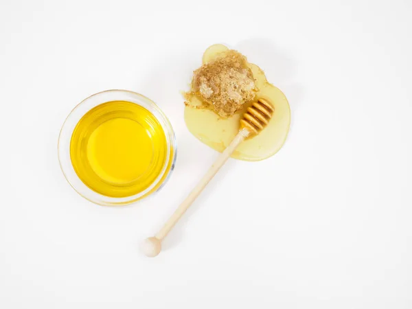 Composición de la miel en un tazón, una cacerola de madera para la miel y una gota de miel extendida en una mesa blanca, panal de abeja —  Fotos de Stock