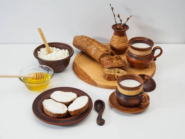 Productos lácteos ecológicos para el desayuno en loza sobre fondo blanco. Miel natural floral y jarra de miel. Leche de granja, sándwich de queso cottage, queso cottage con miel — Foto de Stock