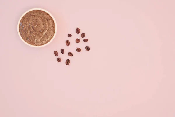 Exfoliante corporal de café natural en un bol blanco y granos de café sobre un fondo rosado. Plano, vista superior, espacio para copiar — Foto de Stock