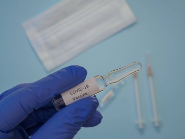 Mavi tıbbi eldiven teslim eden bir adam koronavirüs aşısıyla bir ampul tutuyor.