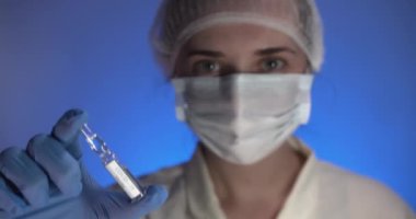 Steril tıbbi eldivenleri ve maskesi olan kadın bir doktor koronavirüs enfeksiyonuna karşı aşısı olan bir ampul taşıyor. Seçici odak